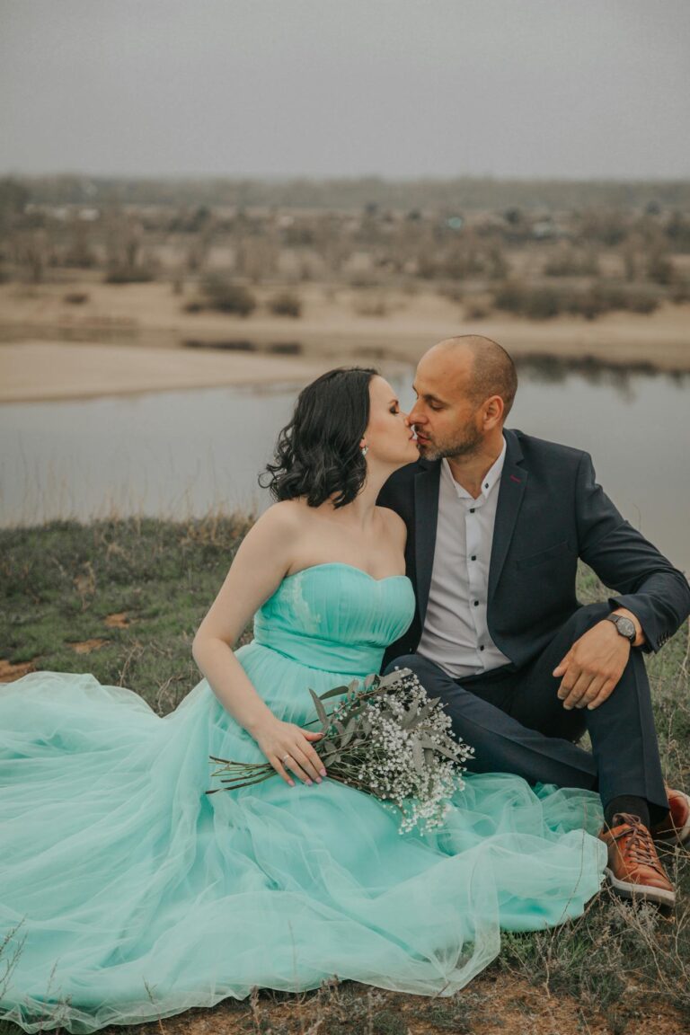 Newlywed couple kissing on river coast on wedding day