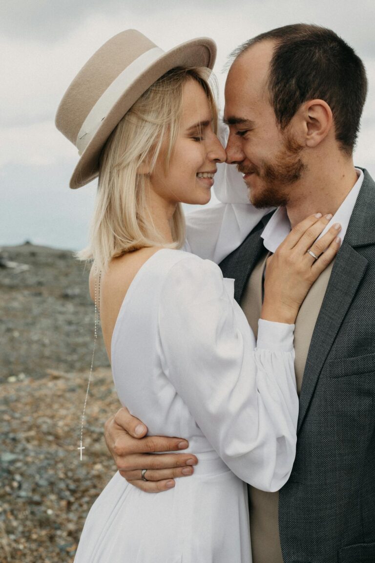 Side view of cheerful unshaven man embracing elegant wife with closed eyes and cross during festive occasion in daylight